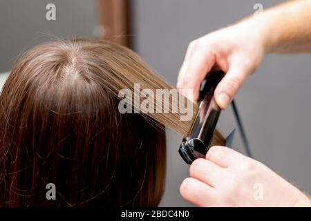 Friseursalon glättet die Haare der Frau mit Haarglättwerkzeug im Friseursalon. Stockfoto