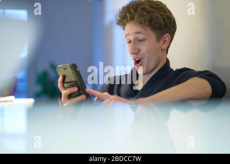 Der junge Mann ist glücklich überrascht, als er sein Handy in seinen Händen betrachtet Stockfoto