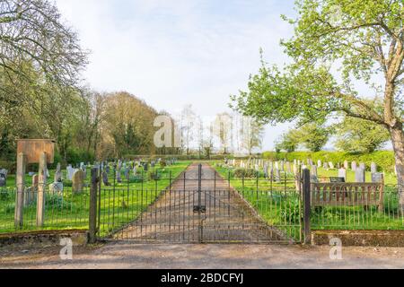 Eingang zum Friedhof mit vorderen Toren mit Parkbank und Bäumen in St Thomas' Church, Perry Green, Much Hadham, Hertfordshire. GROSSBRITANNIEN Stockfoto