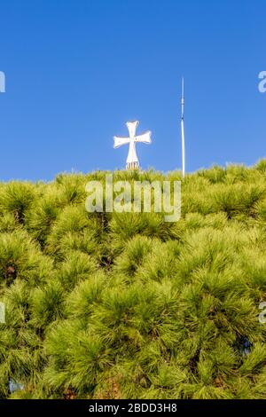 Schönes weißes Kreuz der orthodoxen Kirche des Klosters St. Nikolaus, See Vistonida, Porto Lagos, Xanthi-Region, Nordgriechenland, Kirchturm Teilansicht gegen klaren blauen Himmel, grüne Bäume Stockfoto