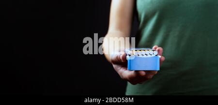 Bieten Sie Rauchen an, eine Packung Zigaretten in der Hand auf einem dunklen Hintergrund mit Platz für Kopien. Stockfoto