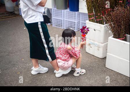 24.01.2020, Singapur, Singapur - EIN kleines Mädchen in Chinatown hält eine Windmühle in der Hand, während sie auf dem Fuß ihrer Mutter sitzt. 0SL200124D024CARO Stockfoto