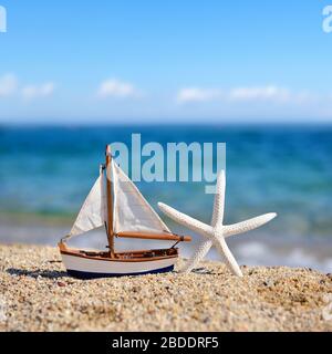 miniatur-spielzeugsegler und Seesterne am Strand vor dem Hintergrund des Meeres und des blauen Himmels Stockfoto