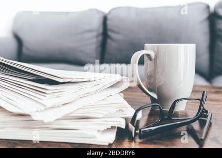 Nahaufnahme von Zeitungen, Kaffeebecher und Brille auf dem Wohnzimmertisch. Stockfoto