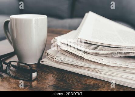 Nahaufnahme von Zeitungen, Kaffeebecher und Brille auf dem Wohnzimmertisch Stockfoto