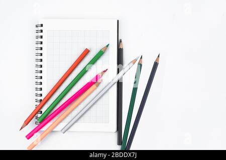 Einige verschiedene farbige Bleistiftkrebse aus Holz, die über und über ein Tagebuch aus weißem Papier verstreut sind