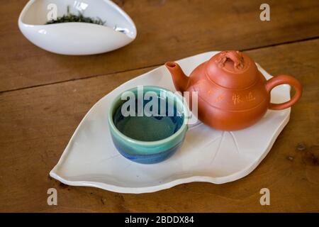 Schöne chinesische Tee Zeremonie mit roten Tontopf und kleine Tasse auf handgefertigten weißen Keramikplatte mit männlicher Hand gesetzt Stockfoto