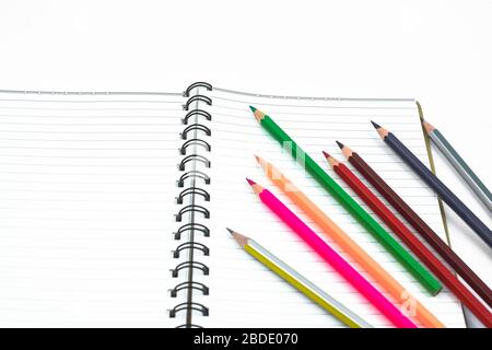 Verschiedene farbige Bleistiftkrebse, die in einer winkten Formlinie vor einem weißen Papiertagebuch platziert wurden Stockfoto