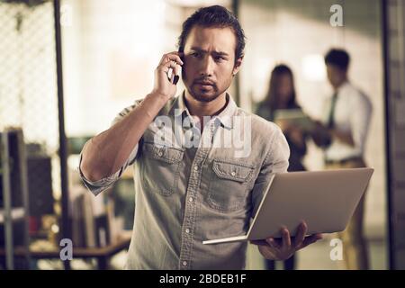 Unternehmer in Asien, der einen Laptop mit Telefon im Büro telefoniert Stockfoto
