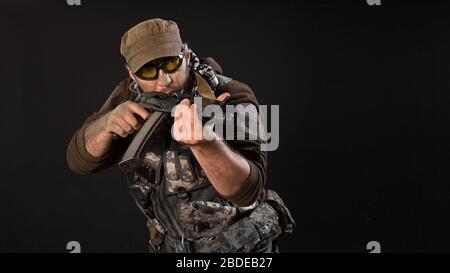 Ein Söldner mit einer Waffe zielt auf den Feind. Nahaufnahme auf dunklem Hintergrund. Modernes privates Armeekonzept. Stockfoto