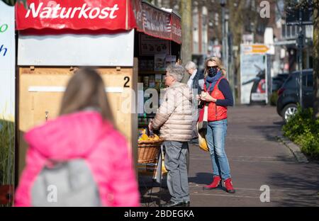 Nordhorn, Deutschland. April 2020. Besucher eines Wochenmarktstandes an einem Stand mit Gesichtsmasken. Auch auf den Wochenmärkten müssen die Fernabstände in der Coronakrise eingehalten werden. Credit: Friso Gentsch / dpa / Alamy Live News Stockfoto