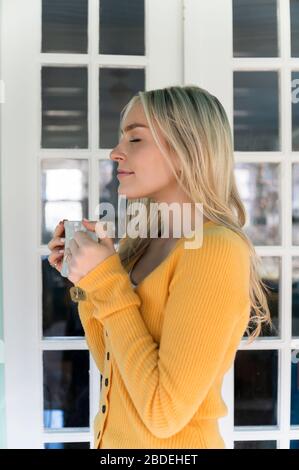 Portrait der Frau in gelben Pullover hält Tasse Stockfoto