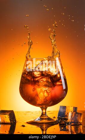 Ein großes Glas Whiskey mit Spray wurde auf schwarzem Glas mit Reflektion fotografiert Stockfoto