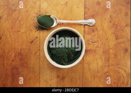 Spirulina in Schüssel und Löffel voll gegen Holz Stockfoto