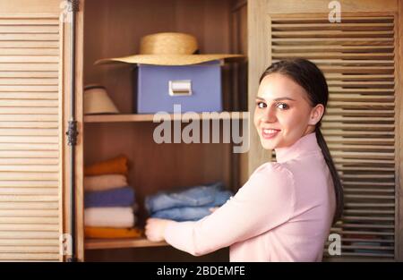 Junge brünette Mädchen falten ihre Kleidung und legen sie in Schrank und Kisten. Nordischer Stil - Minimalismus. Stockfoto