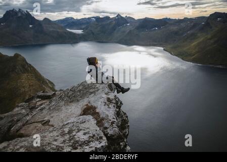 Norwegen, Senja, Mann, der fotografiert sitzt am Rand einer steilen Klippe auf dem Berg Segla Stockfoto