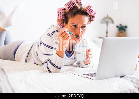 Frau mit Lockenwicklern, die auf dem Bett liegen und sich angucken Notebook Stockfoto
