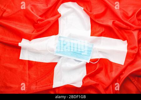 Coronavirus in der Schweiz. Schützende chirurgische Gesichtsmaske auf Schweizer Nationalflaggen. Schweizer Quarantäne, Schutzkoronavirus Symbol des türkischen Arztes Stockfoto