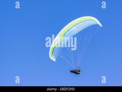 Ein einzelner Gleitschirm in Mittelluft mit einem klaren blauen Himmel mit Raum als Hintergrund. Stockfoto