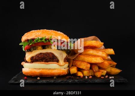 Ein großer klassischer Hamburger mit pommes frites auf schwarzem Steinteller auf schwarzem Hintergrund und Platz für Text Stockfoto