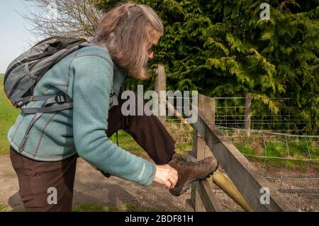 Woman Walker, die ihre Schnürsenkel beim Ausruhen auf einem Tor auf dem Land in der Nähe von Bellingham, Northumberland, England, Großbritannien, binden Stockfoto