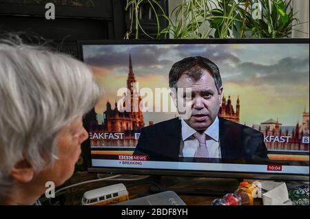 Eine ältere Frau, die Staatsminister für Gesundheit beobachtet, gab Edward Argar ein BBC-Fernsehinterview über Covid-19. Stockfoto