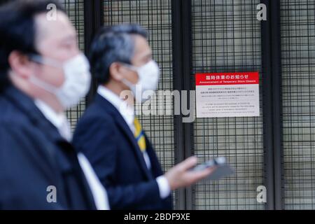 Tokio, Japan. April 2020. Fußgänger, die Gesichtsmasken tragen, gehen an einem Hinweis vorbei, in dem sie die vorübergehende Schließung des Kaufhauses Mitsukoshi in Ginza ankündigen. Einige Läden in Tokio haben beschlossen, ihre Türen vorübergehend zu schließen, nachdem der japanische Premierminister Shinzo Abe die Erklärung eines Ausnahmezustands für die Hauptstadt und sechs weitere Präfektur Japans abgegeben hatte. Credit: Rodrigo Reyes Marin/ZUMA Wire/Alamy Live News Stockfoto