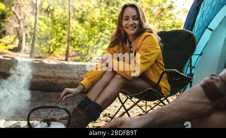 Schöne Frau, die am Lagerfeuer sitzt und ihren Mann betrachtet. Ein Paar auf dem Campen, das außerhalb des Zelts sitzt. Stockfoto