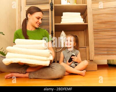 Frau mit kleiner Tochter, die in der Nähe des Schranks sitzt und Handtücher in der Waschküche hält. Gemütliches und sauberes Hauskonzept Stockfoto