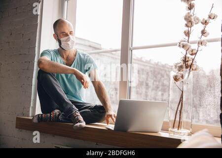 Inspiriert. Junger Mann, der zu Hause Yoga macht, während er unter Quarantäne steht und freiberuflich online arbeitet. Remote-Standort, isoliert. Konzept des gesunden Lebensstils, des Wohlbefindens, während der Coronavirus Pandemie sicher sein. Stockfoto