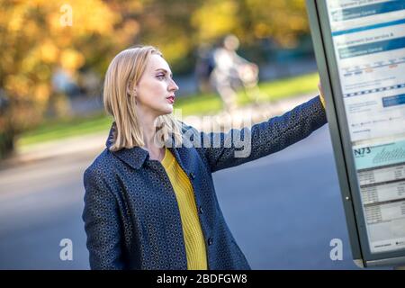 Junge Frau an der Bushaltestelle überprüft den Zeittisch Stockfoto