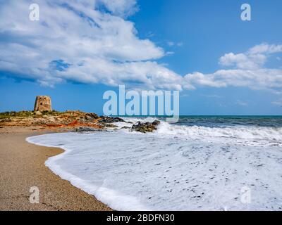 Das Wahrzeichen der Stadt Bari Sardo, der Torre di Barì, ein Turm, der auf einem Felsvorsprung am Strand mit beigem Sand und Meer mit schäumenden Wasser erbaut wurde Stockfoto