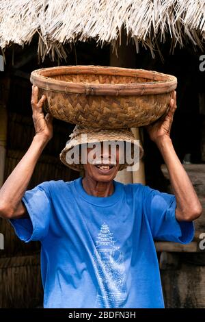 Vertikales Porträt eines traditionellen Gewürzherstellers, der einen Korb auf dem Kopf in Bali, Indonesien, trägt. Stockfoto