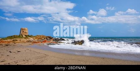 Das Wahrzeichen der Stadt Bari Sardo, der Torre di Barì, ein Turm, der auf einem Felsvorsprung am Strand mit beigem Sand und Meer mit schäumenden Wasser erbaut wurde Stockfoto