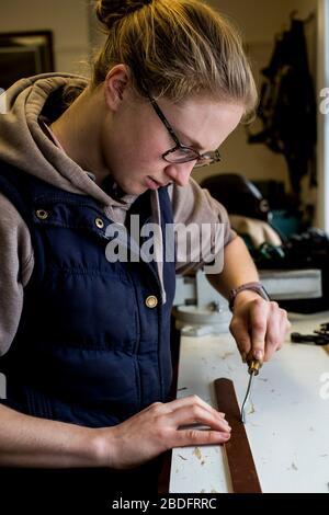 In der Werkstatt stehender Sattler mit Handwerkzeug am Lederriemen. Stockfoto