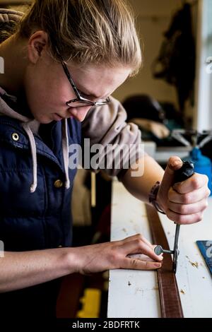 In der Werkstatt stehender Sattler mit Handwerkzeug am Lederriemen. Stockfoto