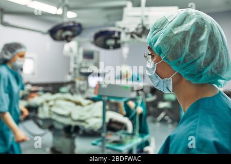 Porträt einer Chirurgen, Operation im Hintergrund. Chirurgie Medizin Konzept. Weibliche Chirurgen, Gleichstellung der Geschlechter, Leben retten. Schönheit und Gesundheit Stockfoto