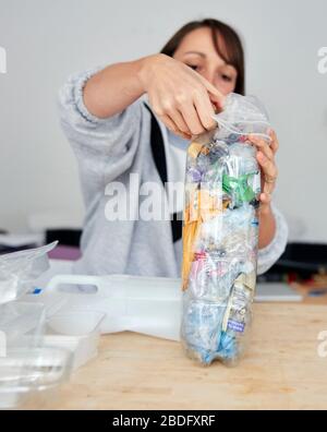 Frau betufft weiche Kunststoffabfälle in große Plastikflaschen, um einen Ökobrick herzustellen, der dann als Bruderblock verwendet werden kann Stockfoto