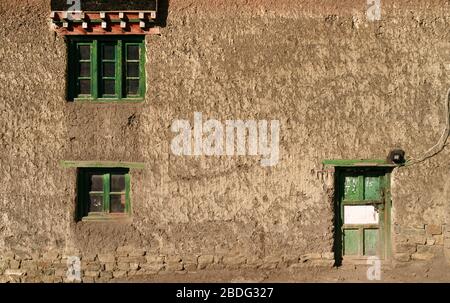 Traditionelles, mit Schlamm geputztes Dorfhaus mit Holzrahmen versehenen Fenstern und Tür an einem sonnigen Morgen im Sommer in Komic, Himachal Pradesh, Indien. Stockfoto