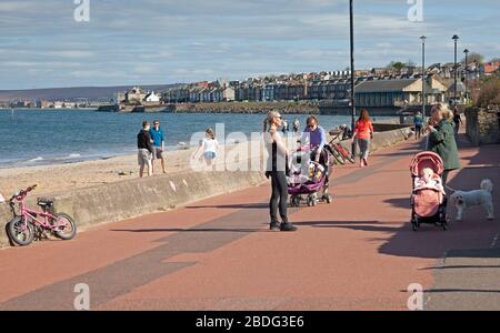 Portobello Beach, Edinburgh, Schottland, Großbritannien. April 2020. 18 Grad und voller Sonnenschein brachten Sonnenanbeter ans Meer, die meisten sozialen Distanzierungen, aber nicht die Menschenmassen, die erwartet würden, wenn es nicht den Coronavirus Lockdown gäbe und die Menschen hauptsächlich spazieren oder sitzen, anstatt auf dem Sand zu liegen. Ein männlicher und weiblicher Polizist auf der Promenade für einen Routinepassgang. Credit: Arch White/Alamy Live News Stockfoto