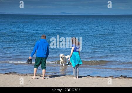 Portobello Beach, Edinburgh, Schottland, Großbritannien. April 2020. 18 Grad und voller Sonnenschein brachten Sonnenanbeter ans Meer, die meisten sozialen Distanzierungen, aber nicht die Menschenmassen, die erwartet würden, wenn es nicht den Coronavirus Lockdown gäbe und die Menschen hauptsächlich spazieren oder sitzen, anstatt auf dem Sand zu liegen. Ein männlicher und weiblicher Polizist auf der Promenade für einen Routinepassgang. Credit: Arch White/Alamy Live News Stockfoto