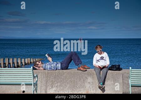 Portobello Beach, Edinburgh, Schottland, Großbritannien. April 2020. 18 Grad und voller Sonnenschein brachten Sonnenanbeter ans Meer, die meisten sozialen Distanzierungen, aber nicht die Menschenmassen, die erwartet würden, wenn es nicht den Coronavirus Lockdown gäbe und die Menschen hauptsächlich spazieren oder sitzen, anstatt auf dem Sand zu liegen. Ein männlicher und weiblicher Polizist auf der Promenade für einen Routinepassgang. Credit: Arch White/Alamy Live News Stockfoto