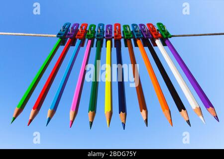 Buntstifte hängen auf farbigen Wäscheklammern auf blauem Hintergrund. Stockfoto