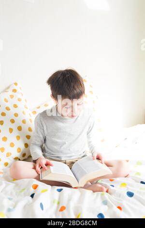 Schuljunge im Bett und Hausaufgaben machen Buch zu Hause lesen. Online-Fernunterricht. Quarantäne. Konzept, das zu Hause bleibt Stockfoto