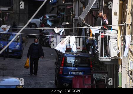 Neapel, Italien. April 2020. Ein Mann mit seinem Kind ist auf dem Balkon, als ein Mann Schutzmasken-Pässe in der Straße im spanischen Viertel (Quartieri Spagnoli) in der Innenstadt trägt. In Italien wird der Sperrverfall weiterhin durch Regierungsdekret erklärt, das ganz Italien zu einem Schutzgebiet zur Bekämpfung der Kovidinfektion 19 erklärt - Coronavirus-Infektion, Schließung von Schulen, öffentlichen Büros und Geschäften. Kredit: Unabhängige Foto-Agentur Srl/Alamy Live News Stockfoto