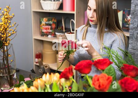 Hübsche Frau Floristin wählt Rosenblätter aus. Die Blondine sammelt einen Blumenstrauß aus perfekten roten Rosen. Stockfoto