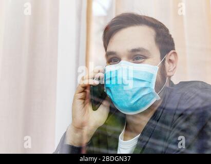 Einsamer Mann in Quarantäne mit Kovid 19 in der Isulation telefonieren mit der Familie, schauen Sie in Fenster. Vorbeugung gegen eine Coronavirus-Pandemie. Mann in Schutz Stockfoto