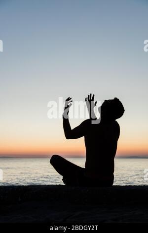 Silhouette eines Mannes, der bei Sonnenuntergang am Strand zu Gott betet Stockfoto