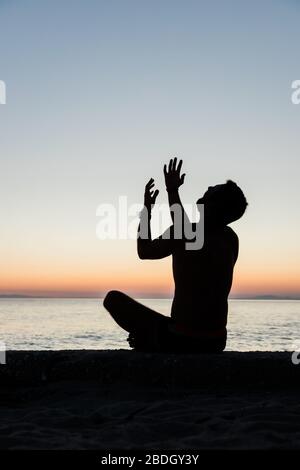 Silhouette eines Mannes, der bei Sonnenuntergang am Strand zu Gott betet Stockfoto