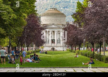 Como, ITALIEN - 4. August 2019: Lokale Menschen und Touristen auf der Viale Guglielmo Marconi in der Nähe des Comer Sees. Tempio Voltiano Museum im Hintergrund. Warme sonne Stockfoto